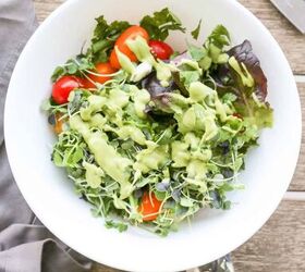 keto vegan avocado dressing recipe gluten free, vegan avocado dressing recipe drizzled over a salad with micro greens and tomatoes in a white bowl with spoons and a napkin