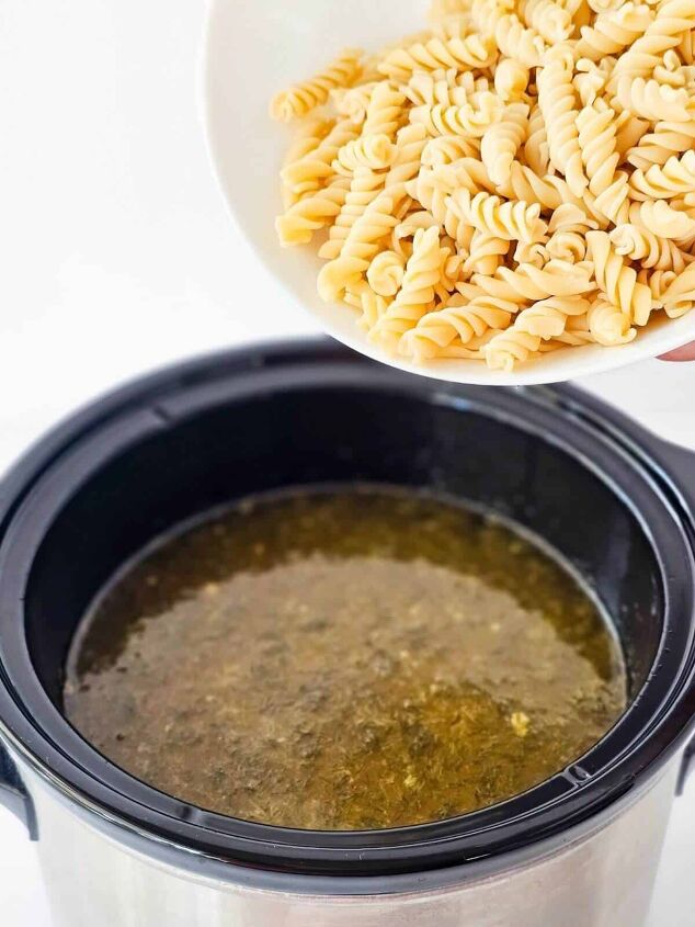 the best ground chicken soup recipe, A bowl of cooked rotini pasta being poured into a slow cooker full of soup