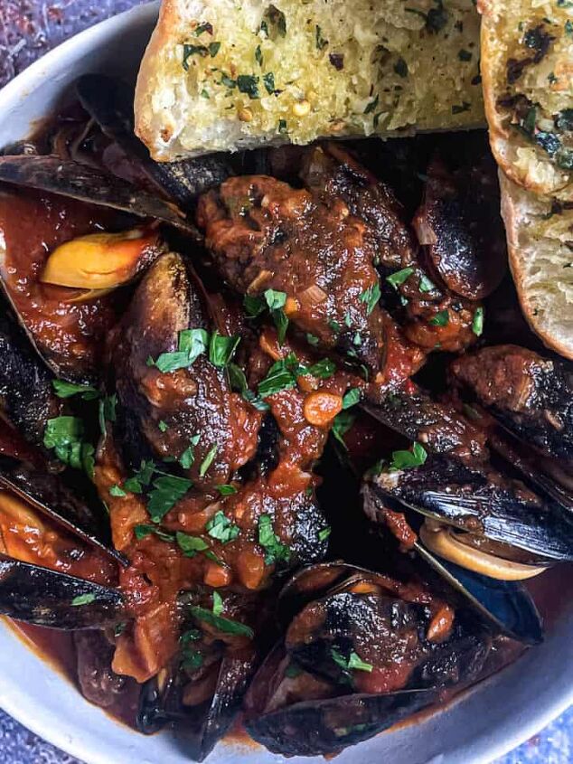 baked mediterranean spot prawns, mussels in tomato sauce in a bowl with garlic bread