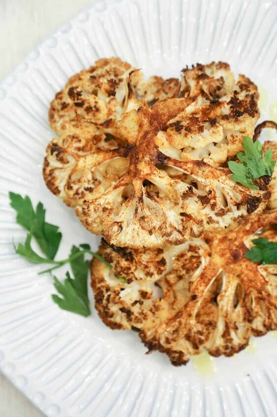 keto air fryer cauliflower steaks, air fryer cauliflower steaks made with Peruvian spice blend on a white plate garnished with parsley and olive oil