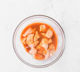 Mixing bowl with chicken pieces in melted butter hot sauce and seasoning