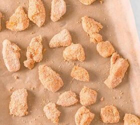 Baking tray lined with parchment paper and filled with marinated chicken pieces that are coated in breadcrumbs