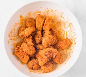 Baked and breaded chicken pieces in a bowl mixed with extra hot sauce