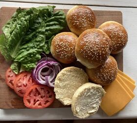 how to make the best brioche hamburger buns from scratch, burger buns with sesame seeds on top laying on a wooden cutting board with lettuce onion cheese and tomato