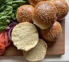 how to make the best brioche hamburger buns from scratch, burger buns with sesame seeds on top laying on a wooden cutting board with lettuce and tomato