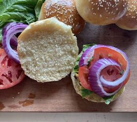 how to make the best brioche hamburger buns from scratch, burger buns with sesame seeds on top laying on a wooden cutting board with lettuce and tomato