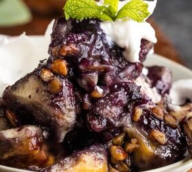 blueberry cobbler bubble up, A close up of a dessert featuring baked purple sweet potatoes topped with nuts whipped cream and a mint leaf garnish served in a white bowl