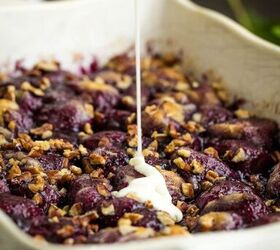 blueberry cobbler bubble up, A baking dish filled with a berry and nut mixture is being drizzled with a white cream sauce