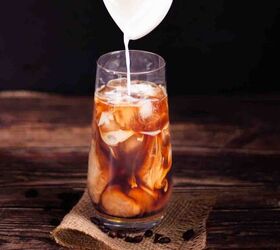 how to make the best iced coffee at home, Cream being poured over coffee and ice cubes in a tall glass