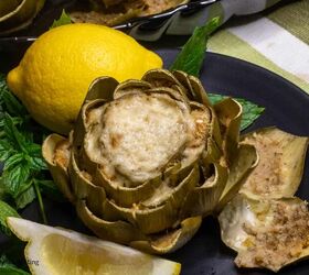 stuffed artichokes made sicilian style, A an artichoke stuffed with bread and cheese on a black plate with lemons and mint