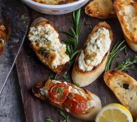 baked ricotta easy italian appetizer, Crostini with a cheese spread on them on a board with herbs and lemons next to a plate of roasted tomatoes