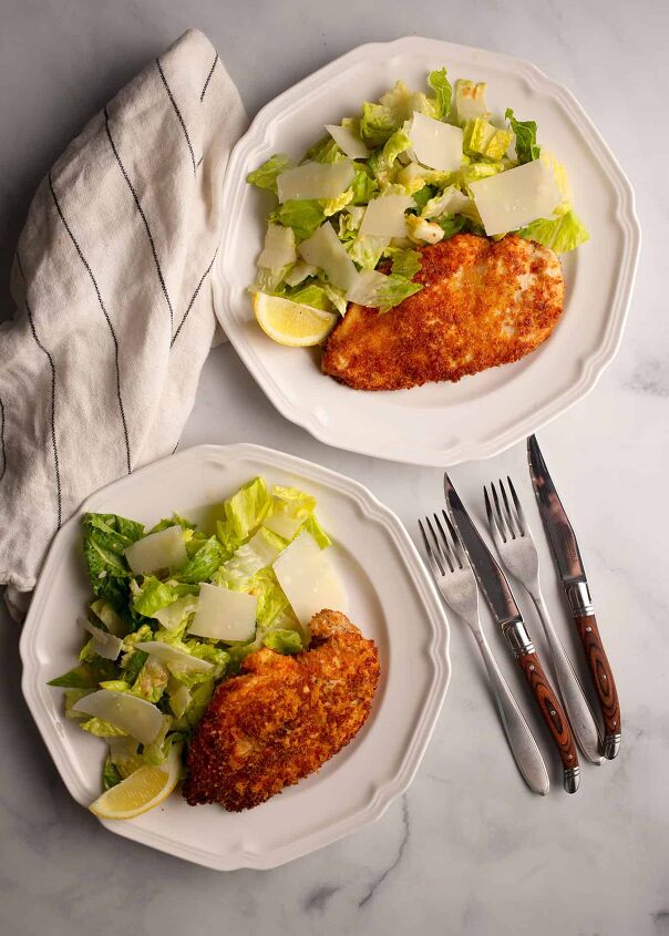 parmesan crusted chicken with caesar salad, Two plates of Parmesan Chicken Caesar Salad with shaved parmesan and lemon slices