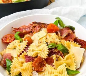 creamy bow tie pasta salad with crispy pancetta, A bowl of bowtie pasta mixed with cherry tomatoes crispy bacon fresh basil and garnished with shaved parmesan In the background a pot with more of the same pasta dish is visible