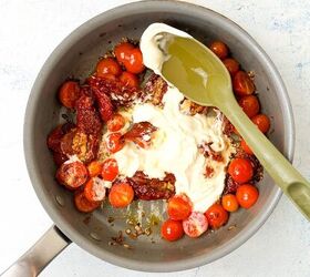 creamy bow tie pasta salad with crispy pancetta, A frying pan with cherry tomatoes sundried tomatoes minced garlic and a dollop of cream cheese A green spatula is resting on the pan ready to stir the ingredients The background is a light textured surface