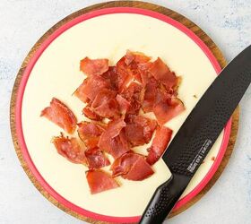 creamy bow tie pasta salad with crispy pancetta, Chopped pieces of pancetta on a round cutting board with a serrated knife placed next to them
