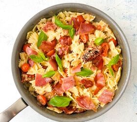creamy bow tie pasta salad with crispy pancetta, A skillet filled with farfalle pasta cherry tomatoes strips of pancetta and fresh basil leaves all mixed with a light sauce The dish is vibrant with red and green hues against a white marble countertop