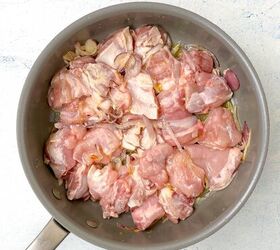 chicken orzo bake one pan family dinner, Raw chicken pieces marinating with sliced onions and garlic in a large silver pan on a light colored surface