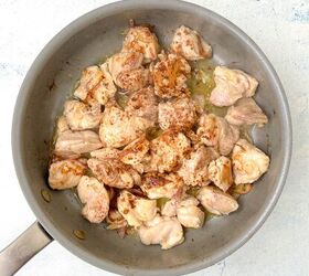 chicken orzo bake one pan family dinner, A frying pan with chunks of chicken cooking lightly browned and sprinkled with spices The pans handle is visible resting on a light blue surface