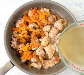 chicken orzo bake one pan family dinner, A pan filled with pieces of cooked chicken sliced apricots and raisins A measuring cup is pouring broth into the pan The background is a light colored countertop