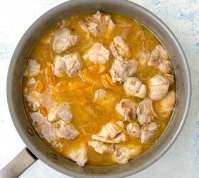 chicken orzo bake one pan family dinner, A pot filled with pieces of chicken simmering in a yellow broth likely seasoned with spices or herbs The liquid is bubbly and the chicken appears tender suggesting its being cooked or stewed The pot is on a light colored surface