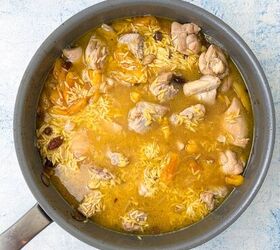 chicken orzo bake one pan family dinner, A saucepan filled with a cooked dish of orzo chicken pieces and orange colored chunks possibly apricots in a light broth The dish is placed on a light blue textured surface