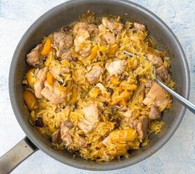 chicken orzo bake one pan family dinner, A pot filled with cooked orzo mixed with pieces of chicken and sliced yellow dried apricots A spoon rests inside the pot which sits on a light blue textured surface The dish appears to be savory and well seasoned