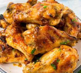 garlic butter chicken wings oven baked, A plate filled with crispy golden brown chicken wings garnished with chopped herbs The wings are glazed giving them a shiny appetizing appearance The plate is set on a light surface with sprigs of fresh parsley nearby