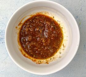 garlic butter chicken wings oven baked, A white bowl filled with a thick brown marinade or sauce reminiscent of the flavors in garlic butter chicken wings containing visible herbs and spices sits on a light blue textured surface