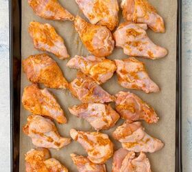 garlic butter chicken wings oven baked, Raw garlic butter chicken wings marinated in seasoning are evenly spaced on a baking tray lined with parchment paper ready for cooking The tray is set on a light blue and white textured surface