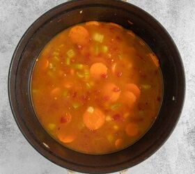coconut curry soup, A black pot filled with vegetable broth containing carrots onions celery and diced tomatoes
