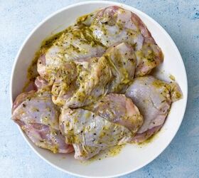 sheet pan chicken thighs and veggies, Raw chicken thighs marinated in a green herb mixture rest in a white bowl on a light blue surface