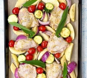 sheet pan chicken thighs and veggies, A baking tray filled with raw chicken thighs slices of potato zucchini cherry tomatoes red onion wedges and sage leaves all seasoned and ready for roasting on parchment paper