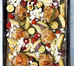 sheet pan chicken thighs and veggies, A baking tray filled with roasted chicken thighs potato wedges cherry tomatoes zucchini slices and red onion all topped with crumbled feta cheese and sage leaves