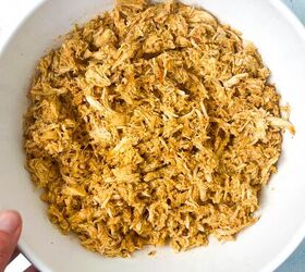 how to make shredded chicken in crockpot, A person holds a white bowl filled with seasoned shredded chicken on a light blue surface