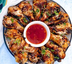 easy soy garlic chicken wings recipe, A plate of grilled soy garlic chicken drumsticks artfully arranged in a circle around a small bowl of red dipping sauce The chicken is garnished with chopped herbs and sesame seeds set against a light blue background
