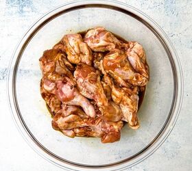 easy soy garlic chicken wings recipe, A glass bowl filled with marinated raw chicken wings rests on a light gray surface The marinade with hints of soy and garlic gives the wings a glossy reddish brown appearance