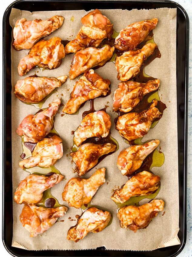 easy soy garlic chicken wings recipe, Soy garlic chicken wings coated in sauce are arranged on a parchment lined baking tray ready for cooking The wings appear marinated with a reddish glaze and are evenly spaced on the tray