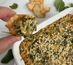 spinach and crab dip, Spinach and crab dip in a white casserole dish with someone holding a cracker that has the dip on top