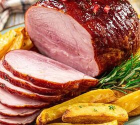 the 3 ingredient ham glaze recipe that changes everything, The image features sliced glazed ham garnished with red berries and rosemary served alongside roasted potato wedges on a plate In the background there is a checkered cloth and a bowl of sauce
