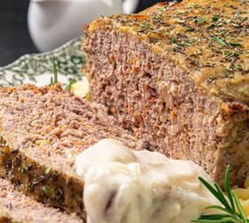 homemade meatloaf with creamy onion gravy, Close up of a sliced meatloaf with herbs on top served with creamy mashed potatoes and gravy A gravy boat is in the background on a decorative green and white plate A sprig of rosemary adds a touch of garnish