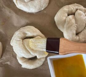soft sourdough pretzels overnight recipe, Three sourdough pretzels lay on a parchment paper lined baking sheet as they get brushed with egg wash