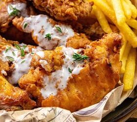 how to make buttermilk fried chicken, Close up of a basket filled with crispy fried chicken topped with a white sauce and garnished with fresh herbs served alongside golden French fries on paper liners