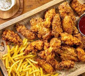 how to make buttermilk fried chicken, A wooden tray filled with crispy fried chicken pieces and golden french fries accompanied by a small bowl of dark red dipping sauce A salt dish with a spoon is visible in the corner placed on a wooden table