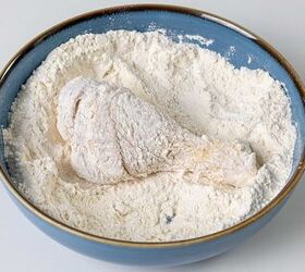 how to make buttermilk fried chicken, A chicken drumstick coated in flour rests in a blue bowl filled with flour ready for cooking