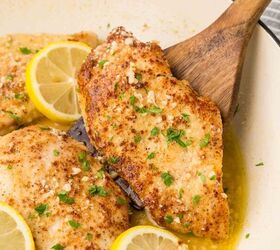 parmesan lemon chicken, chicken in a white pan with a wooden spoon lifting a piece of chicken