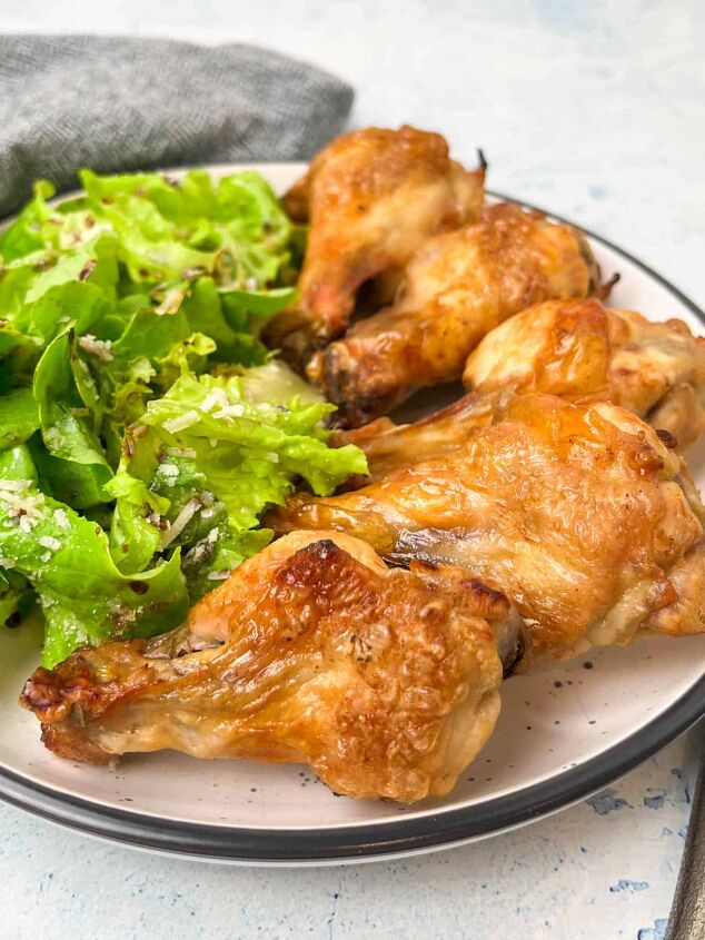 crispy salt and vinegar chicken wings recipe, A plate with crispy baked chicken wings and a side of fresh green salad garnished with grated cheese A gray napkin is placed next to the plate set on a light blue background
