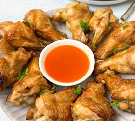 crispy salt and vinegar chicken wings recipe, A plate of crispy chicken wings arranged in a circle around a small bowl of red dipping sauce garnished with chopped herbs Another plate with more wings is partially visible in the background
