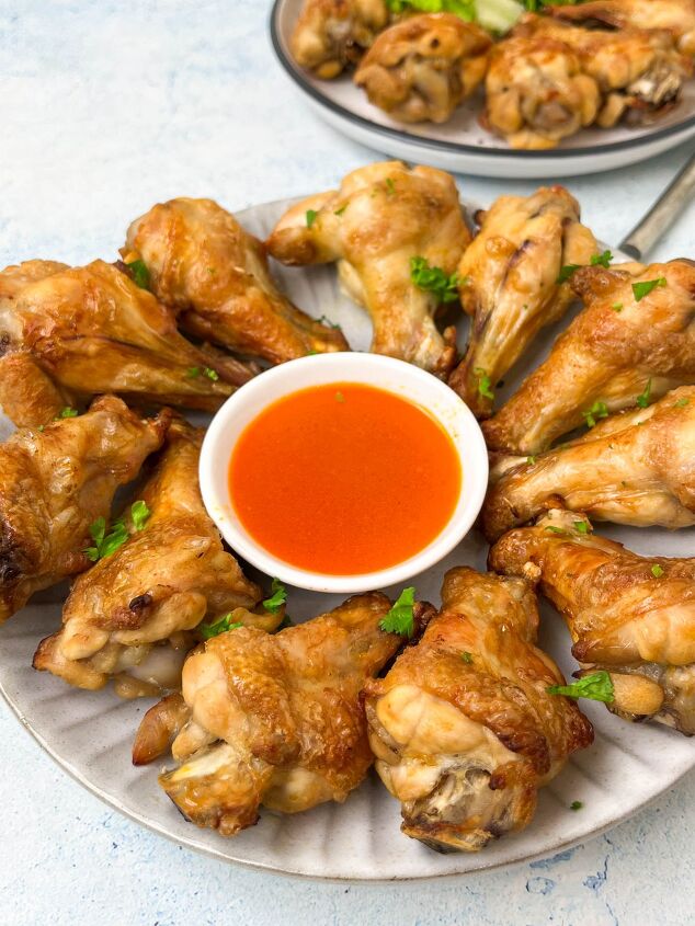 crispy salt and vinegar chicken wings recipe, A plate of crispy chicken wings arranged in a circle around a small bowl of red dipping sauce garnished with chopped herbs Another plate with more wings is partially visible in the background