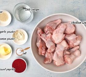 crispy salt and vinegar chicken wings recipe, A top view image of raw chicken wings in a bowl surrounded by small dishes containing white vinegar sugar garlic powder onion powder butter salt and sweet paprika Each ingredient is labeled in text The background is a light blue surface