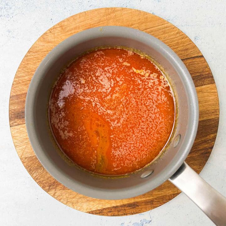 crispy salt and vinegar chicken wings recipe, A saucepan filled with rich bubbly salt and vinegar marinade sits on a round wooden cutting board The sauce appears to be thick with visible textures on the surface suggesting a simmering or reduction process